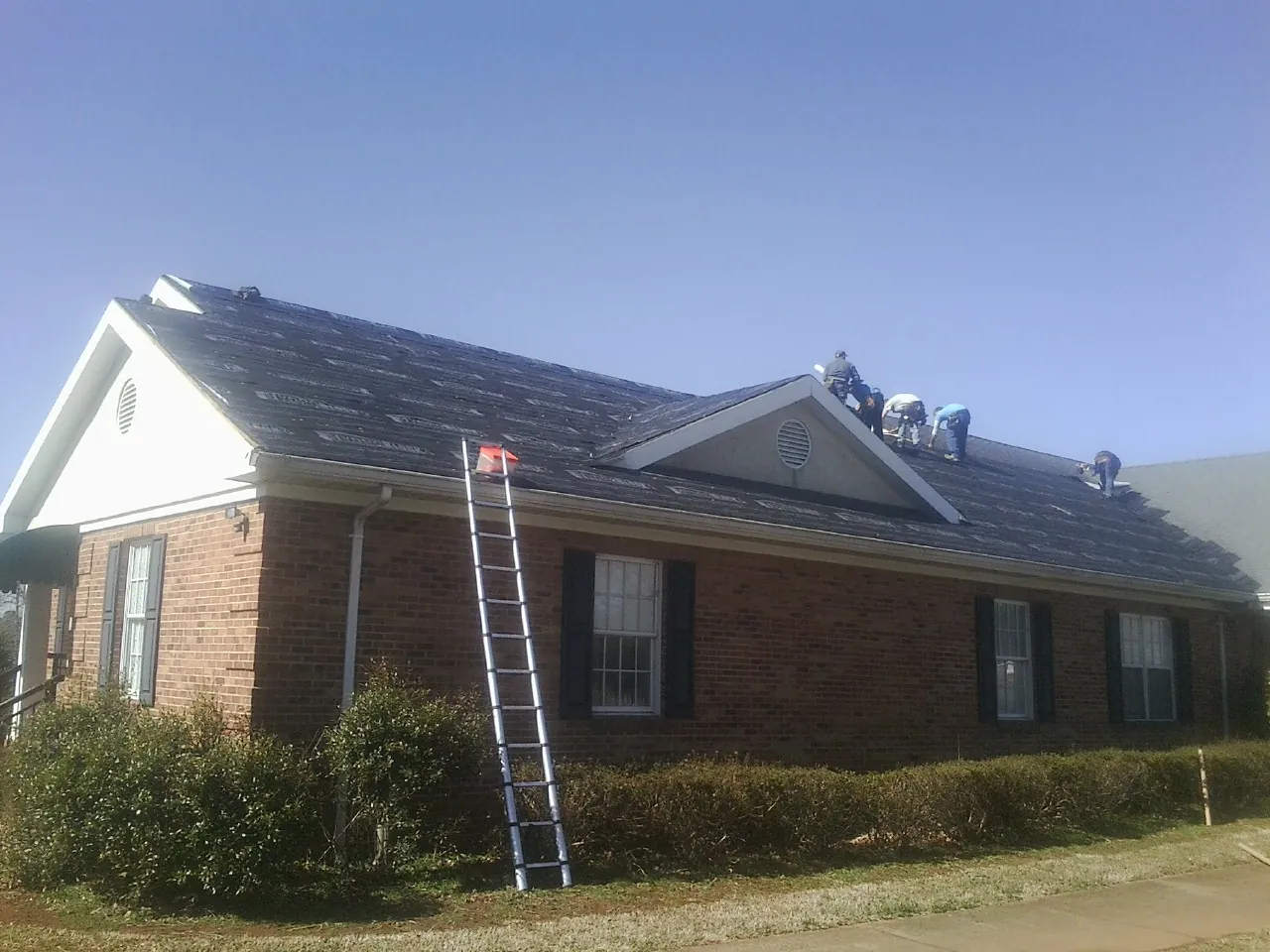 Crew tearing shingles off a brick ranch roof with a ladder set — Emergency Roof Repair work by our crew in Salisbury Mills