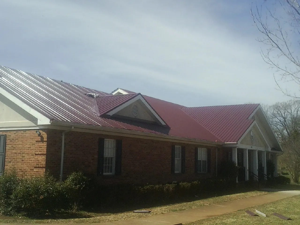 Red metal roof with gabled entries on a long brick building, from a Hail Damage Roof Repair job in Salisbury Mills