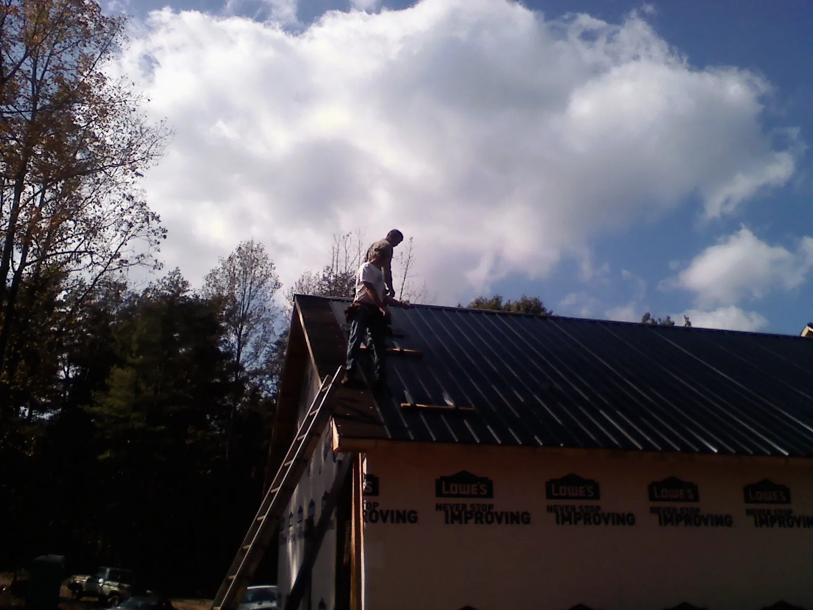 Roofer fastening dark metal panels high against a cloudy sky, from a Roof Inspection job in Salisbury Mills