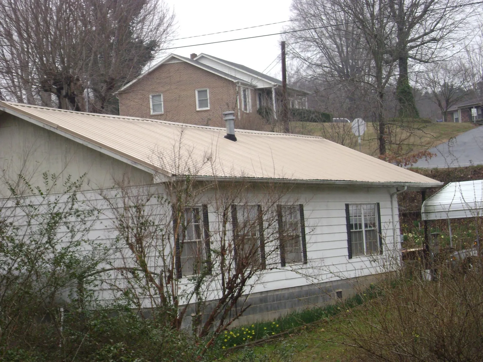 Tan metal roof on a white sided house set into a hillside — Commercial Roofing by Roofing Brothers in Salisbury Mills